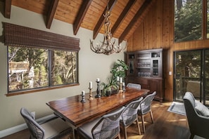 A dining area with a wooden table, wicker chairs, a chandelier, and a view of the outdoors.