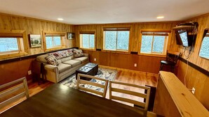 A cozy cabin interior with a sofa, a small table, and a TV mounted on the wall.
