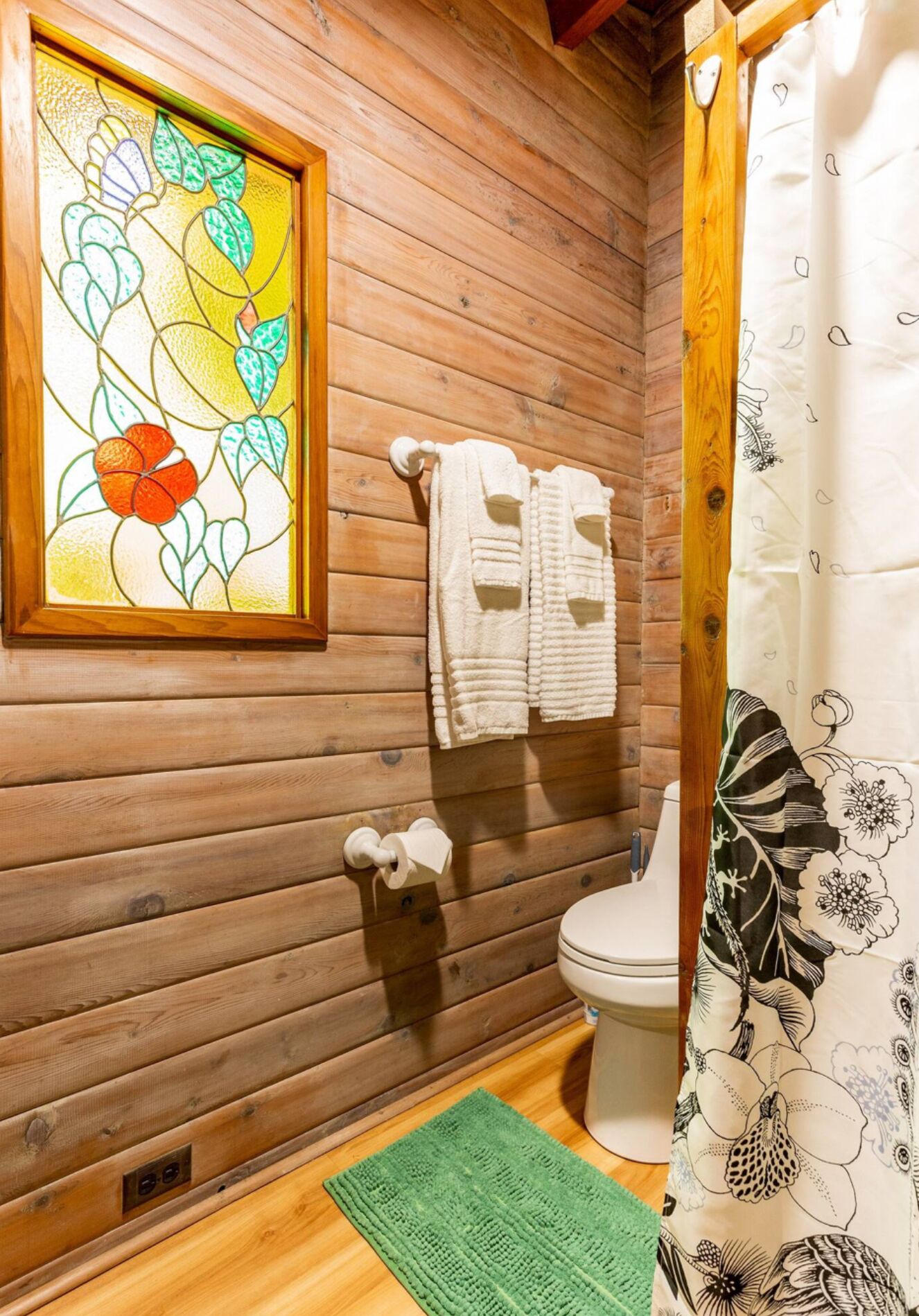 Een houten badkamer met een vakantiehuisje, een glas-in-loodraam, toilet en douchegordijn.