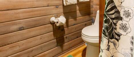 Baño de cabaña de madera con ventana de vitral, inodoro y cortina de ducha.
