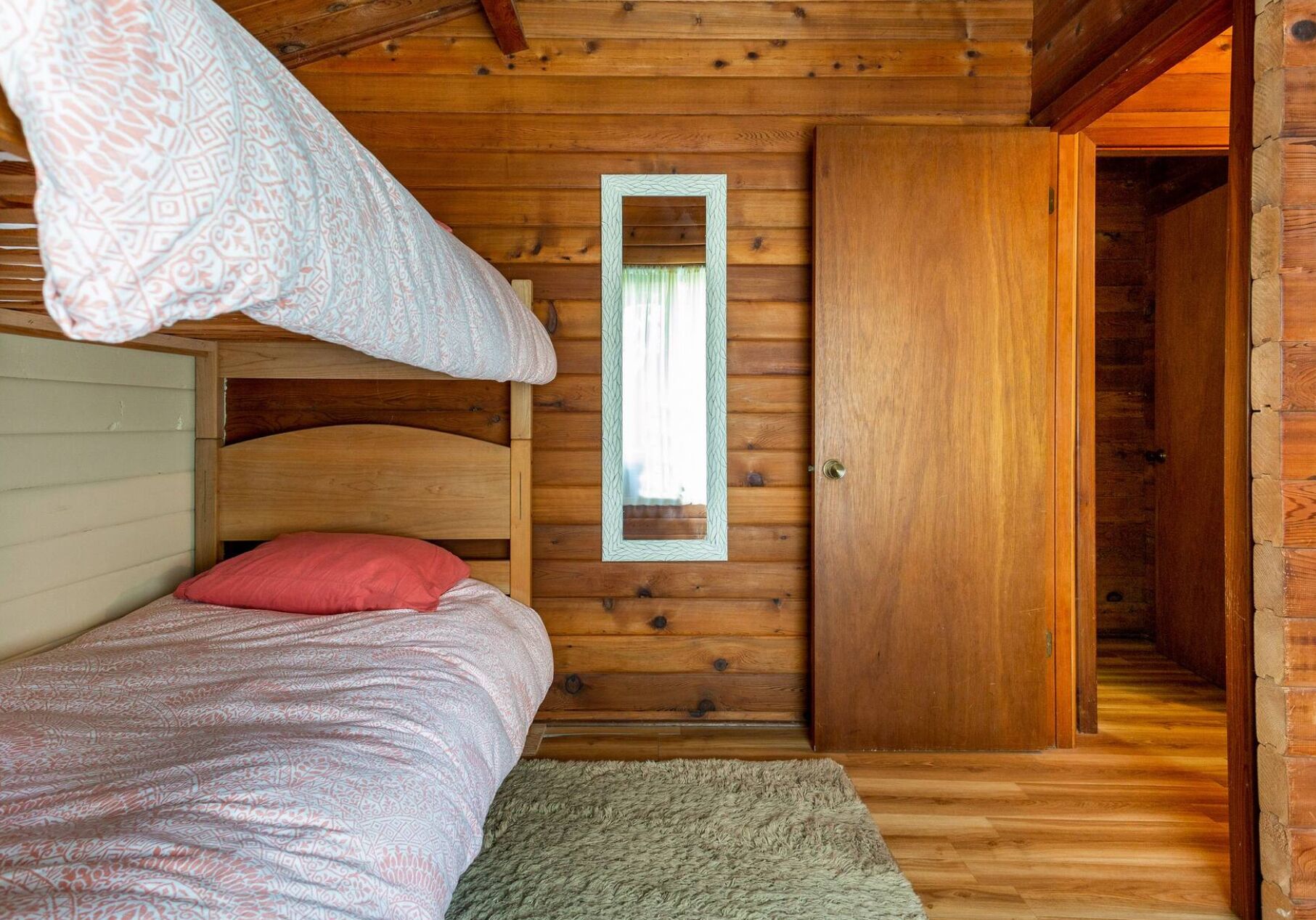 Une pièce de cabane en bois avec un lit superposé, un miroir et une porte donnant sur une autre pièce.