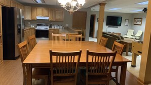 Een ruime keuken met houten kastjes, een eettafel met stoelen, een kroonluchter en een zithoek met een bank en fauteuils.
