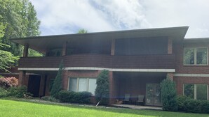 Een twee verdiepingen tellend bakstenen huis met een plat dak, een overdekte veranda en een verzorgd gazon.