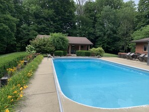 A rectangular swimming pool with a concrete deck, surrounded by lush greenery and a brick building in the background. - 5 BR, 4 baths, Pool, HotTub, Family Friendly, near Louisville KY, Private (Fredericksburg)