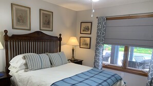 Een netjes opgemaakt bed met een blauw-wit geruit deken, een houten hoofdbord en twee ingelijste foto's aan de muur.