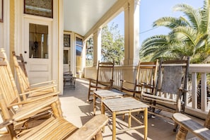 A covered porch with wooden furniture, including chairs and a table, and a view of palm trees. - Historic mansion, 2 blocks to Forsyth Park (Savannah)