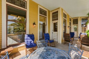 A covered porch with multiple seating areas, including chairs and a table, and a decorative metal railing.
