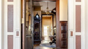 A hallway with a wooden floor, a rug at the entrance, and a staircase leading to another room.