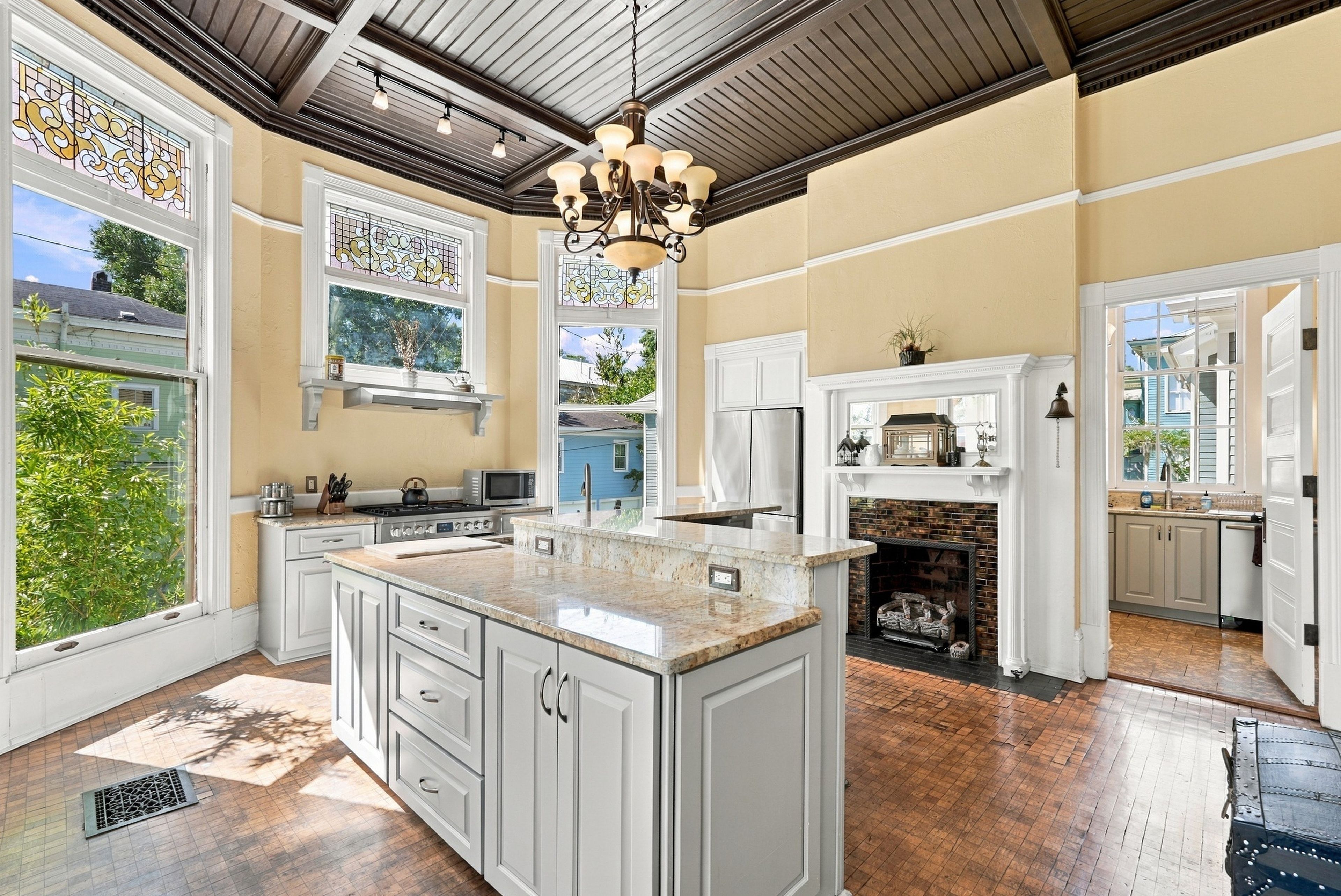 A spacious kitchen with a large island, white cabinetry, and a brick fireplace.