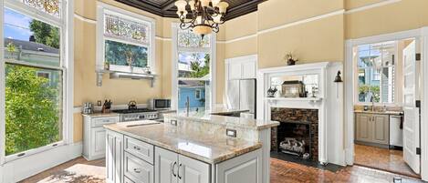 A spacious kitchen with a large island, white cabinetry, and a brick fireplace.