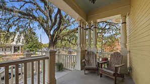 A covered porch with wooden chairs and a table, a railing, and a view of a house and trees.