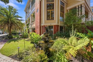 A multi-story building with a central courtyard featuring a tiered fountain, surrounded by lush greenery and palm trees.