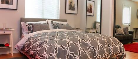 A bedroom with a bed, a nightstand, a mirror, and a window.