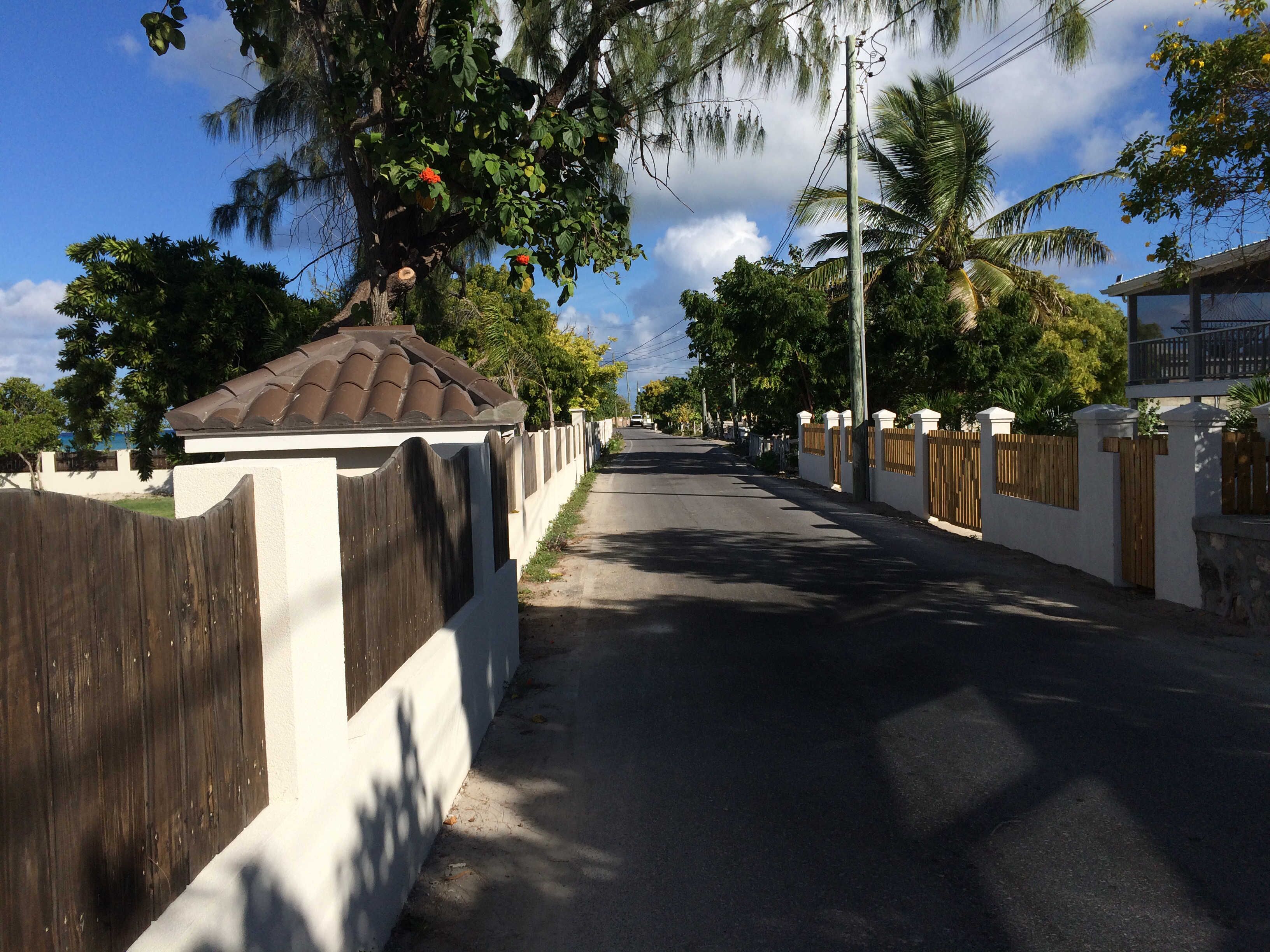 Une rue résidentielle avec une maison blanche, une clôture en bois et un ciel dégagé.