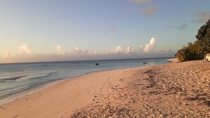 Ein sandiger Strand mit Fußabdrücken und einigen Booten im Wasser.