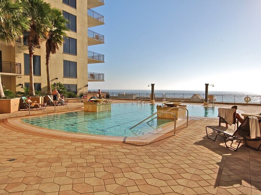 A swimming pool with lounge chairs and a view of the ocean.