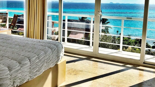Une chambre avec une grande fenêtre donnant sur une plage et l’océan.