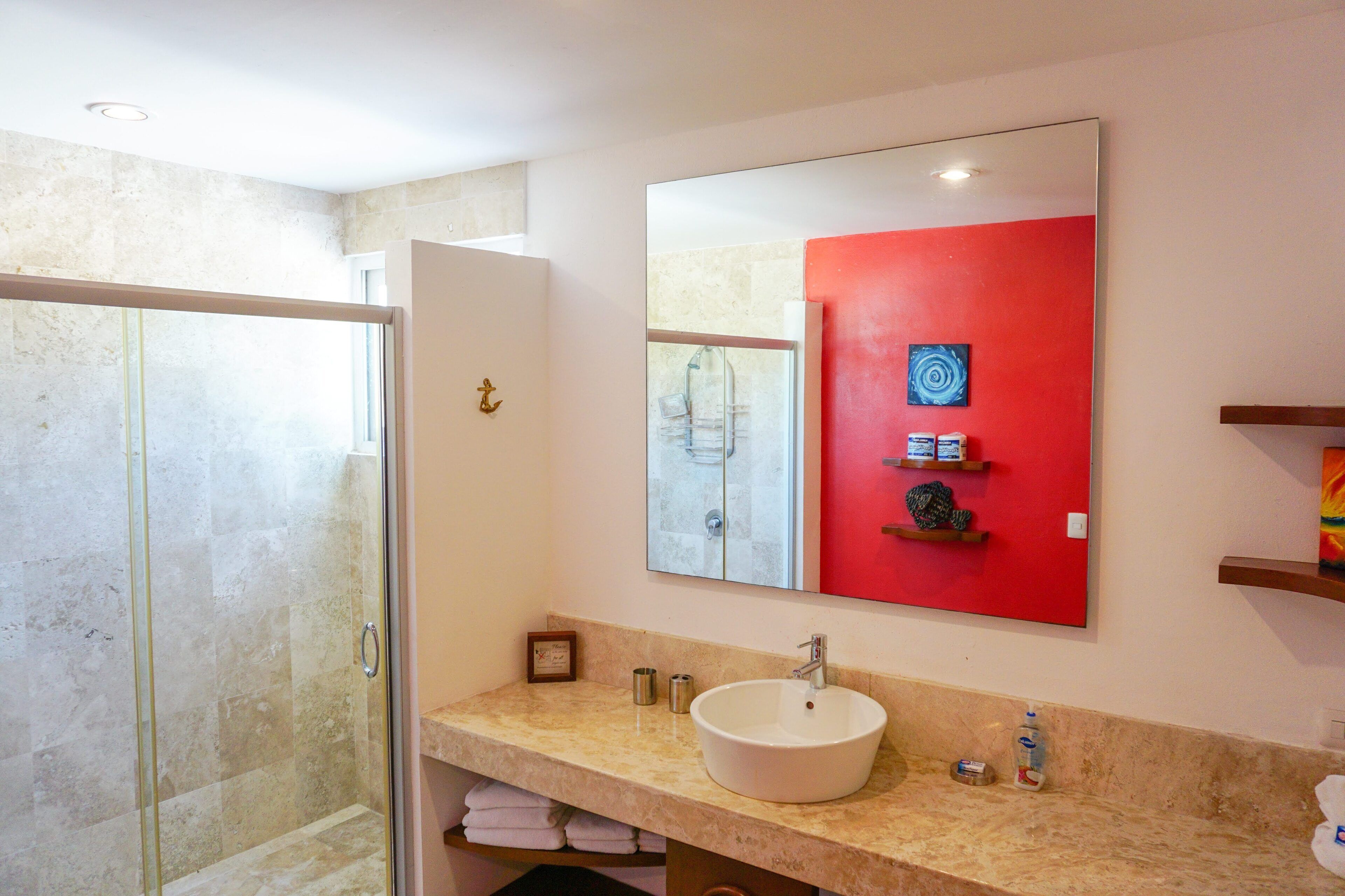 A bathroom with a glass shower enclosure, a white sink, and a red accent wall.