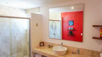 A bathroom with a glass shower enclosure, a white sink, and a red accent wall.