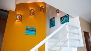 Un escalier avec une rampe blanche et des garde-corps en corde, un mur jaune et deux tableaux.