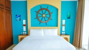 Une chambre d’hôtel avec un grand lit, un grand volant de navire en bois accroché au mur et deux tables de chevet avec des lampes.