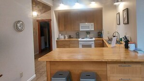 Una cocina con una isla grande, armarios de madera, un microondas y un fregadero. Hay dos taburetes en la isla y un reloj en la pared.