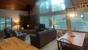 Interior acogedor de una cabaña con chimenea, comedor y ventanas grandes.