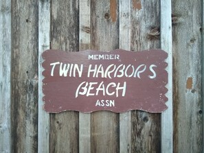 Sään kuluttama puinen taulu, jossa lukee: ”MEMBER TWIN HARBOUR’S BEACH ASSN”.