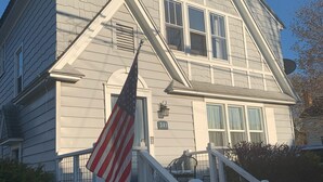 Une maison à deux étages avec un porche à l’avant, un drapeau et une boîte aux lettres.