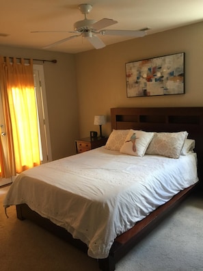A bedroom with a bed, a ceiling fan, a nightstand with a lamp, and a painting on the wall.