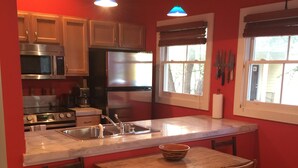 Una cocina con armarios de madera, electrodomésticos de acero inoxidable, una isla central con sillas y una ventana con vistas.
