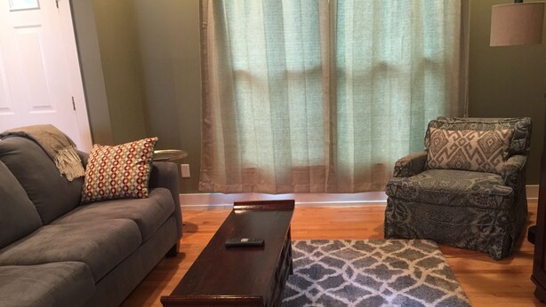 Una sala de estar con un sofá gris, un sillón estampado y una mesa de centro de madera.