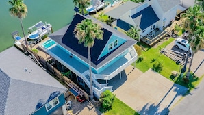 A multi-story house with a pool, a dock, and a boat.
