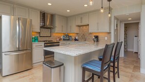 A modern kitchen with stainless steel appliances, a central island with bar stools, and pendant lighting.