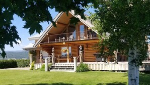 Puinen mökki, jossa on parveke, kuisti ja hyvin hoidettu nurmikko.