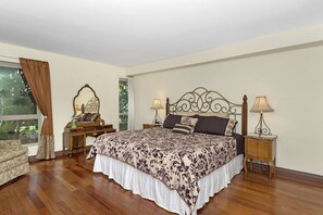 Un dormitorio con una cama grande, cabecera de madera, dos mesitas de noche con lámparas, un aparador y una ventana con cortinas.