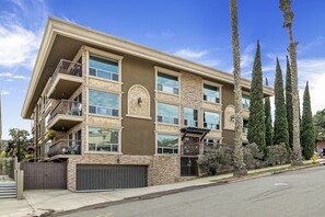 Un edificio de varios pisos con balcones, un garaje y árboles altos.