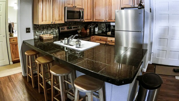 Una cocina con armarios de madera, un refrigerador de acero inoxidable, un microondas, un lavamanos y una zona con taburetes de bar.