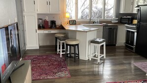 Una cocina moderna con armarios blancos, una isla central con taburetes, horno empotrado y un ventanal grande.