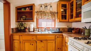 Une cuisine avec des meubles en bois, une cuisinière, un évier et une fenêtre agrémentée de rideaux à carreaux.