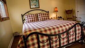 Un lit avec une couvre-lit à carreaux et un cadre en métal noir, une lampe sur une table de chevet et un tableau encadré au mur.