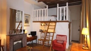 Ein gemütliches Wohnzimmer mit freiliegenden Holzbalken, einem Kamin, einem roten Sessel und einem Holztisch.