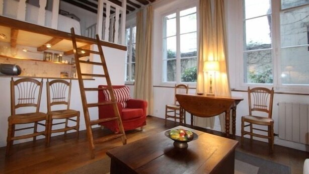 Ein gemütliches Wohnzimmer mit einer Holzleiter, einem roten Sofa und einem Esstisch mit Stühlen.