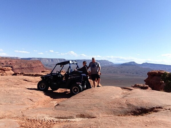 A desert landscape with a dune buggy parked on a rocky outcrop.