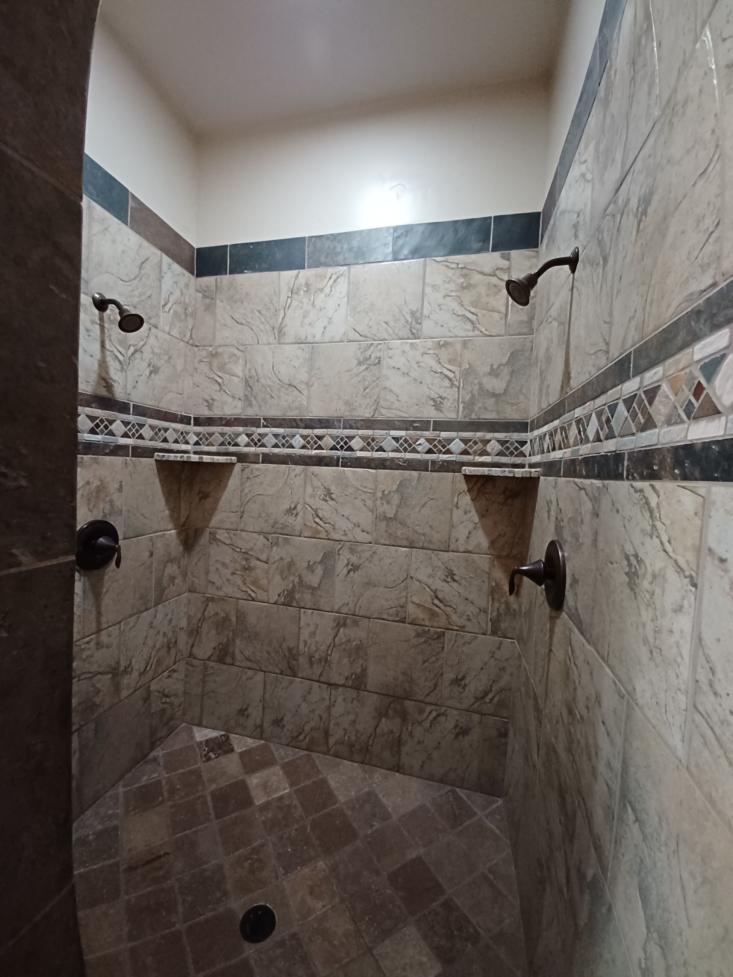 A shower with a tiled floor and walls, featuring a geometric pattern border.