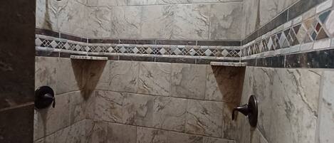 A shower with a tiled floor and walls, featuring a geometric pattern border.
