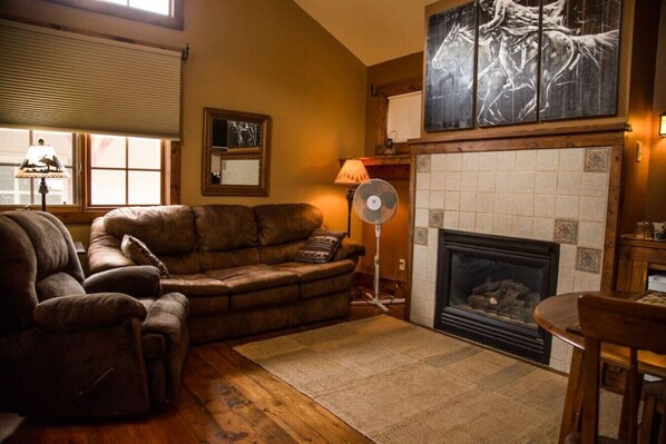 A cozy living room with a leather sofa, a fireplace, and a large abstract painting above it.