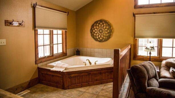 Un baño con una bañera grande, suelo de madera y una ventana con persianas.