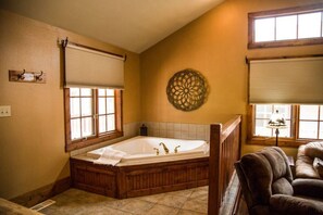Une salle de bain avec une grande baignoire, un plancher en bois et une fenêtre avec des stores.