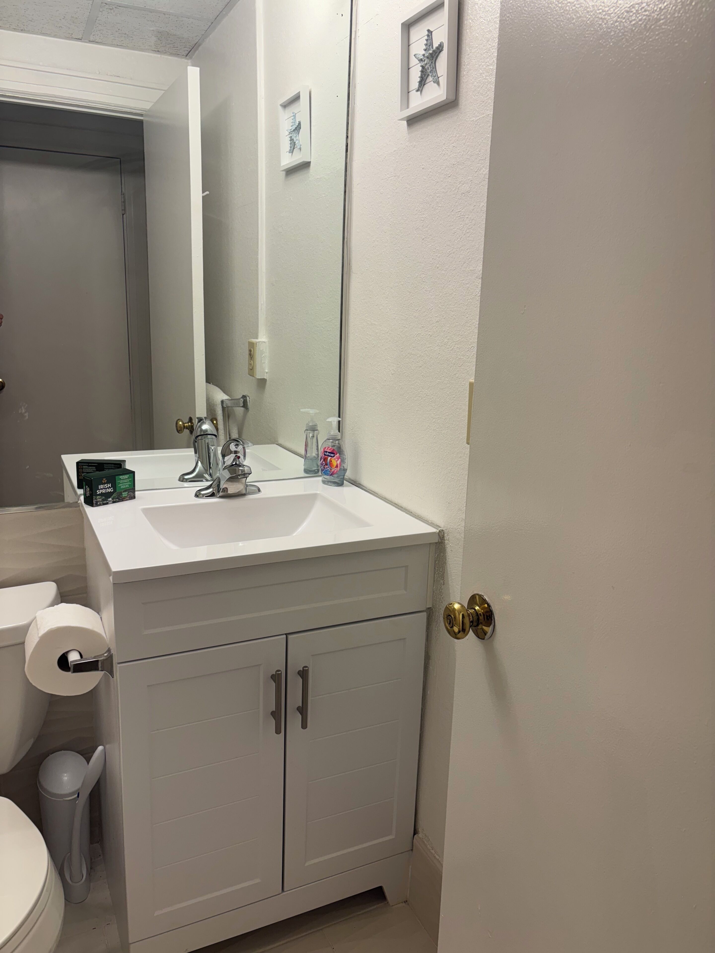 A bathroom with a white sink, a mirror, a toilet, and a trash can.